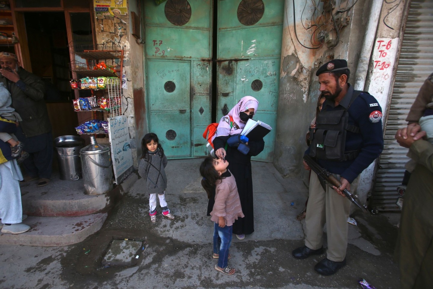 Ein Polizist in Pakistan steht Wache, während einem Kind ein Polio-Impfstoff verabreicht wird.