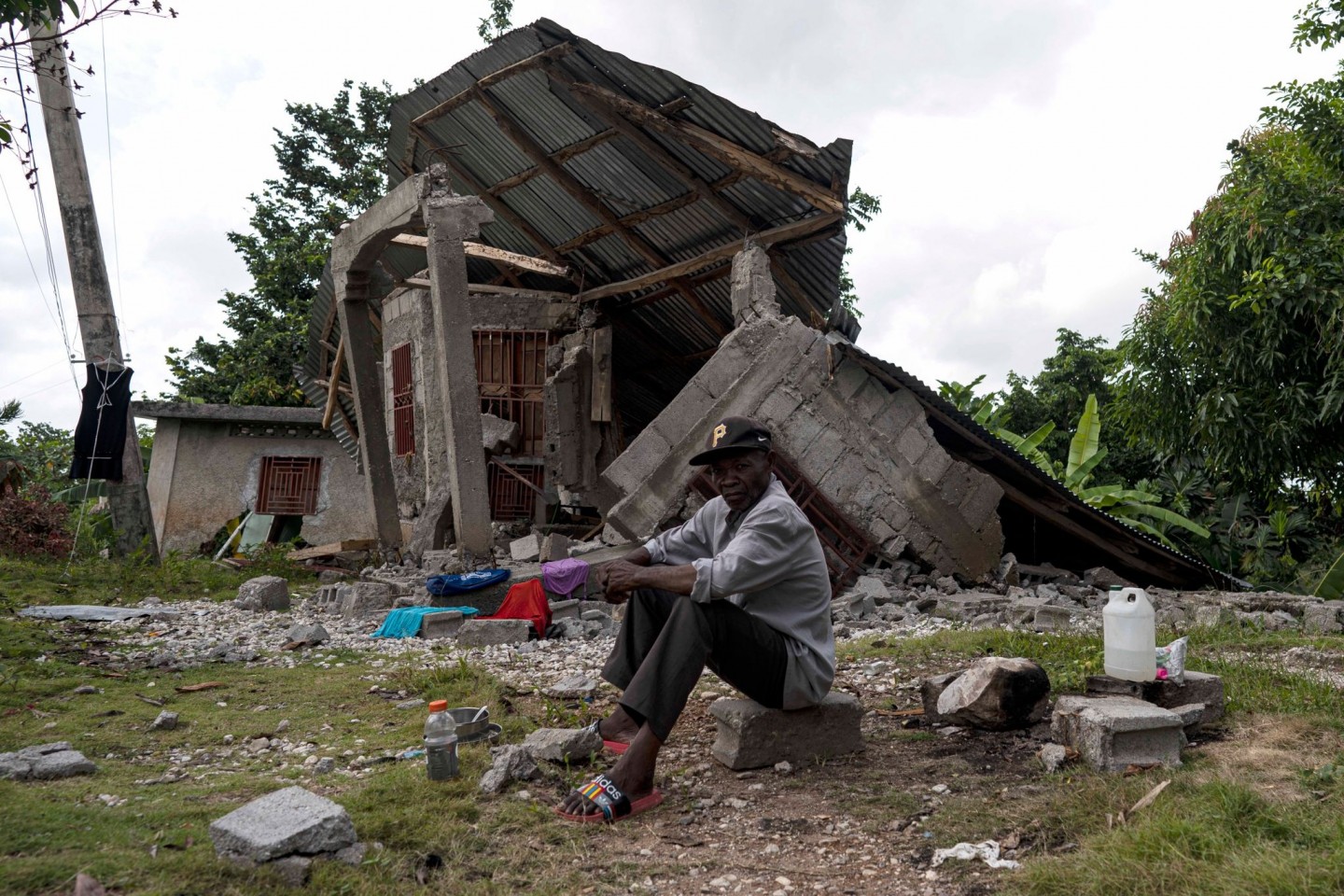 Ein Mann sitzt vor einem zerstörten Haus in Haiti.