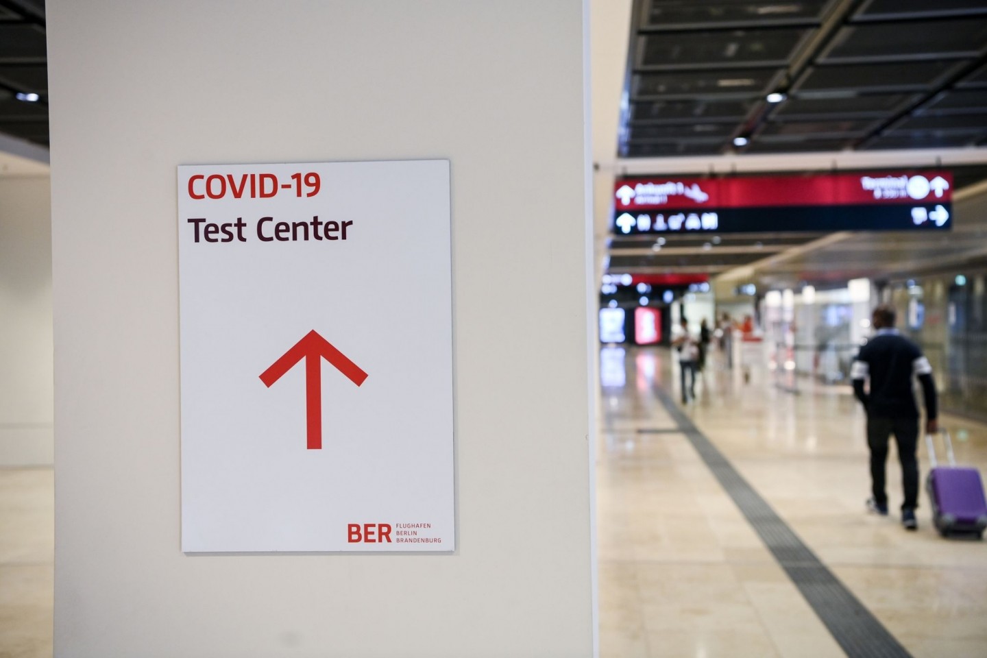Ein Reisender geht im Flughafen Berlin-Brandenburg (BER) mit einem Koffer nahe eines Hinweisschildes mit der Aufschrift «Covid-19 Test Center».