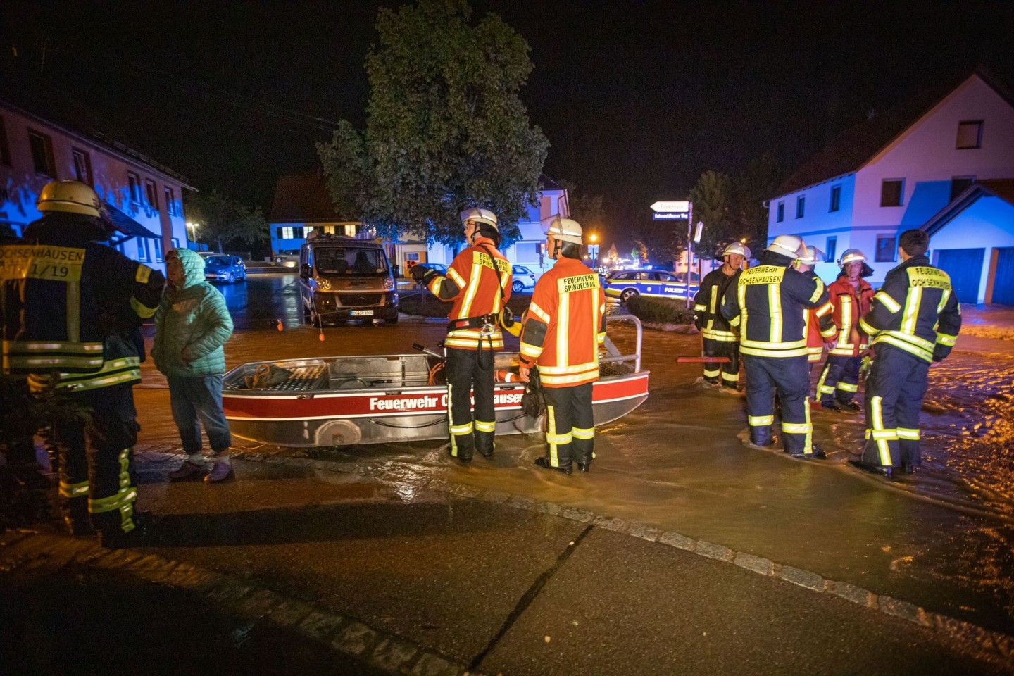 Feuerwehrleute im Kreis Biberach stehen neben einem Feuerwehrboot auf einer Straße in den Fluten eines heftigen Unwetters.