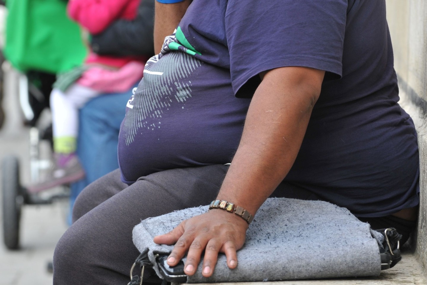 Ein Übergewichtiger sitzt auf einer Steinbank.