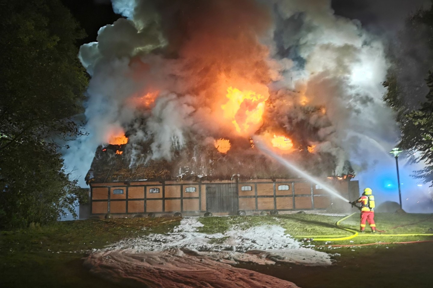 Feuerwehrleute löschen das Feuer in der mit Reet gedeckten Museumsscheune.