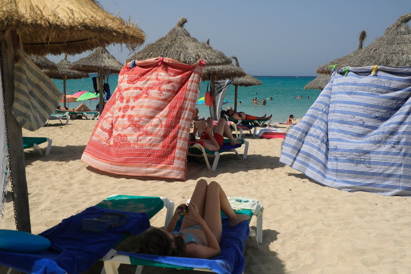 Menschen schützen sich bei extremer Hitze mit Strandtüchern vor der Sonne am Strand von Arenal.