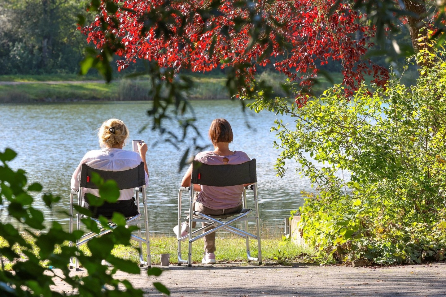 Zwei Frauen sitzen im baden-württembergischen Ertingen an einem See in der Sonne.