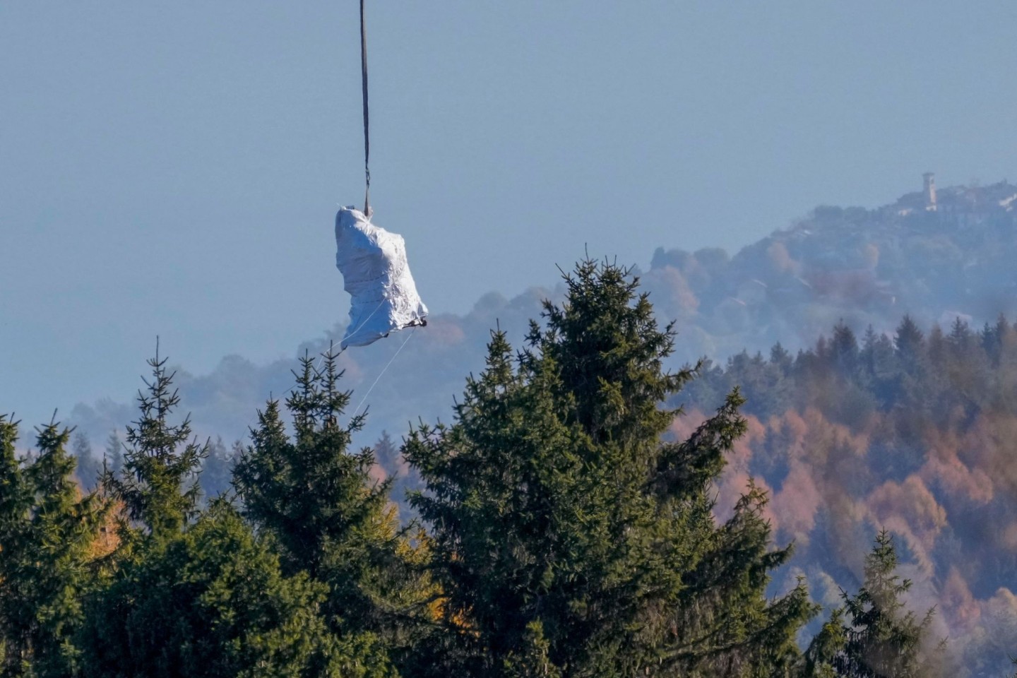 Ein Hubschrauber der italienischen Feuerwehr fliegt die in weiße Planen gehüllte Kabine der abgestürzten Mottarone-Seilbahngondel vom Lago Maggiore ins Tal.