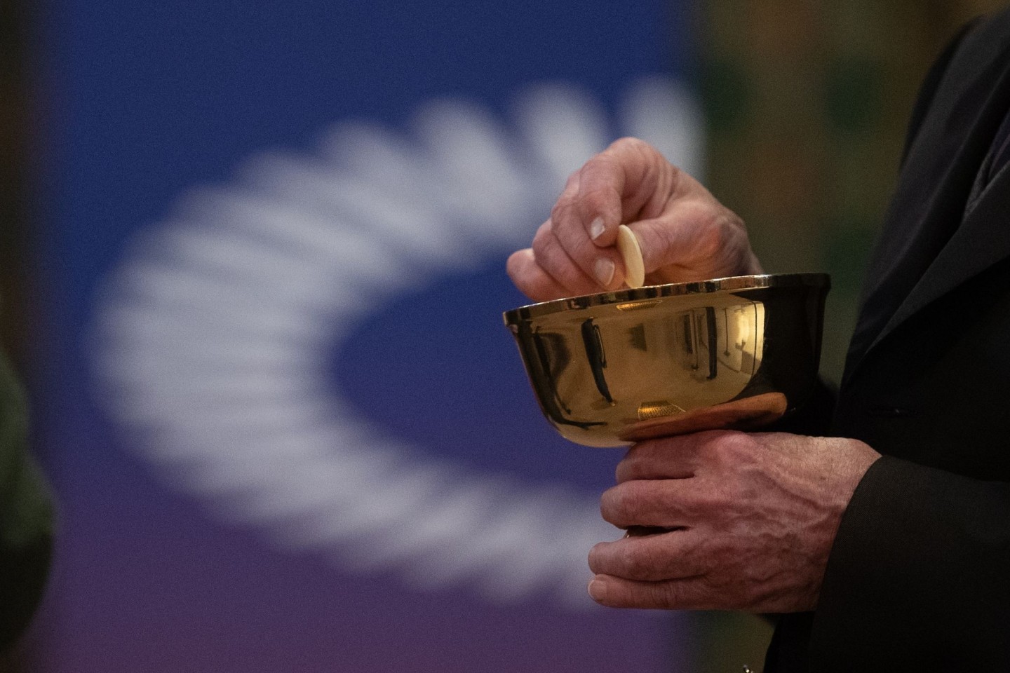 Ein Mitglied der Kirchengemeinde hält während eines Gottesdienstes mit Abendmahl im katholischen Dom St. Bartholomäus vor dem Logo des ÖKT eine Oblate in der Hand.