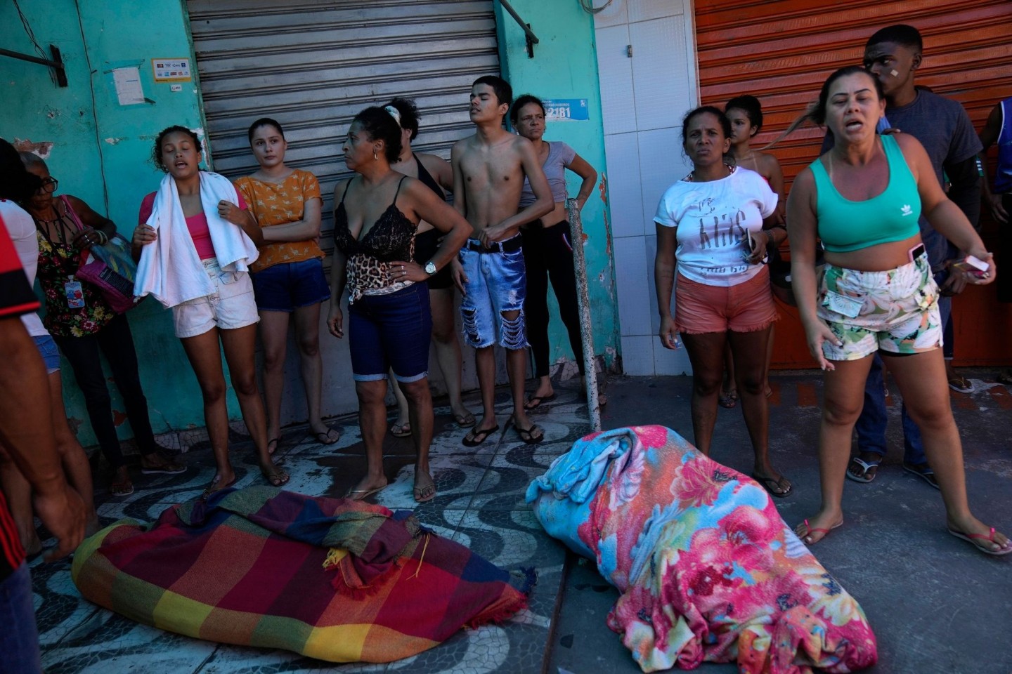 Frauen und Männer stehen um in Decken eingewickelten Leichen nach einem Polizeieinsatz in der Favela Complexo do Alemao.