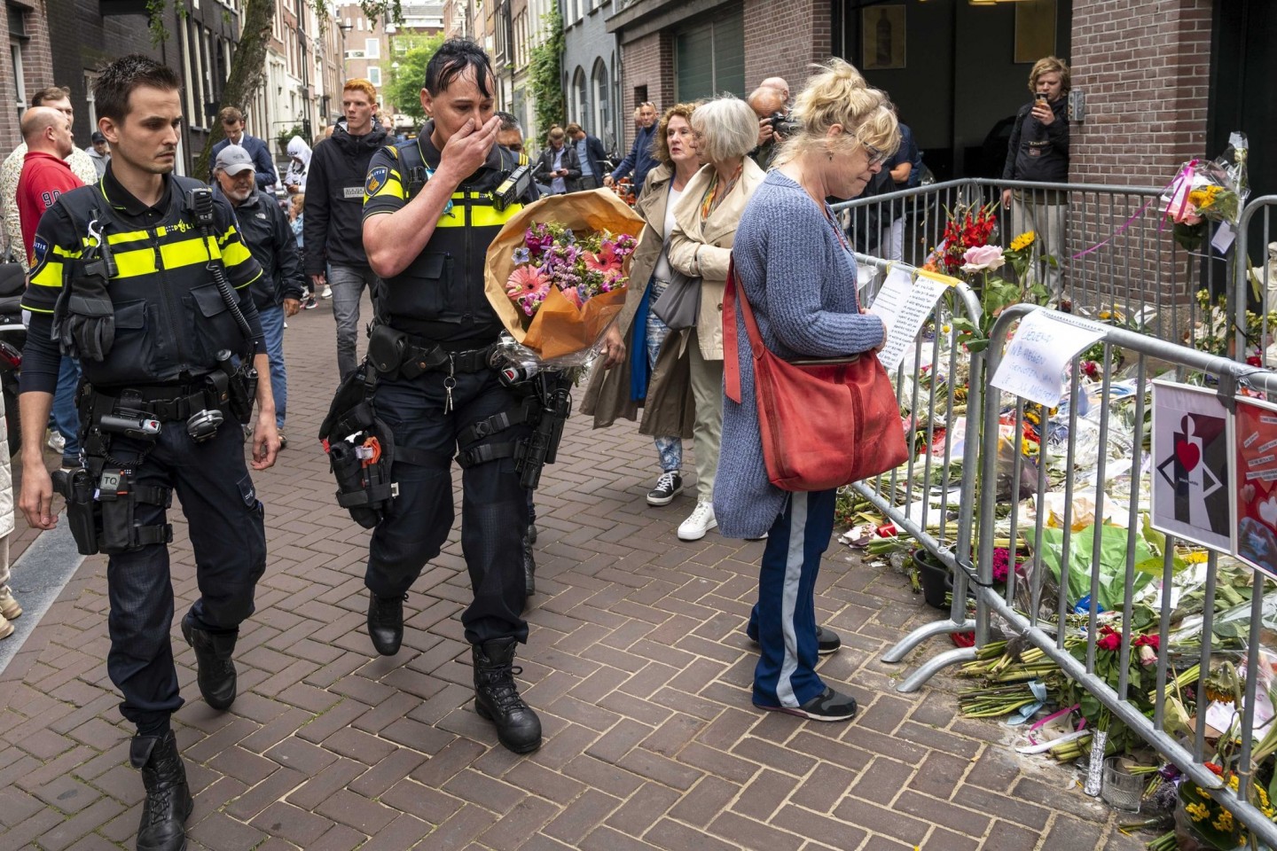 Polizisten bringen einen Blumenstrauß zu dem Blumenmeer für den Reporter Peter R. de Vries in der Leidswarsstraat.