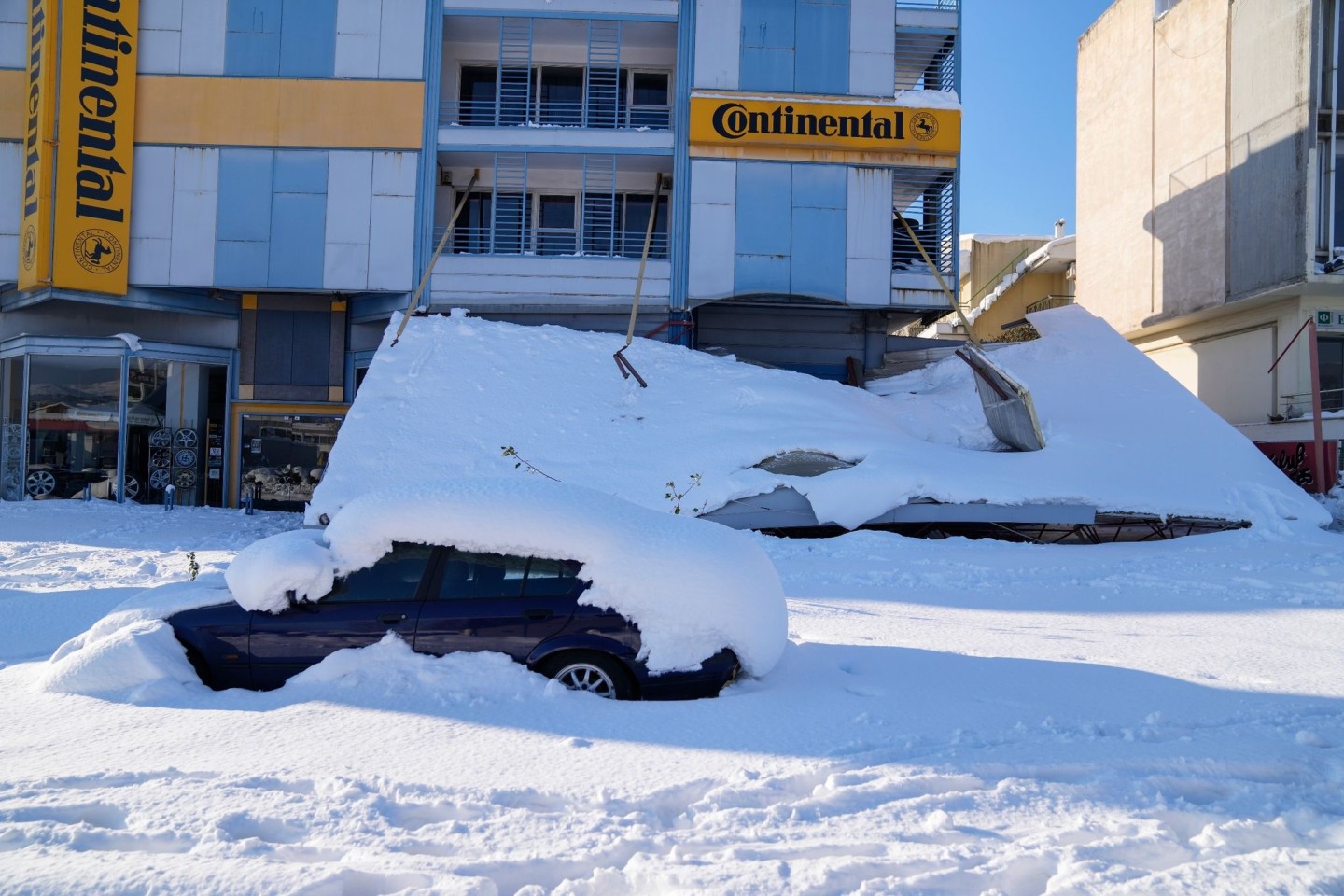 Ein schneebedecktes Auto steht vor einem beschädigten Gebäude. Über dem Großraum Athen waren ungewöhnlich starke Schneefälle niedergegangen.