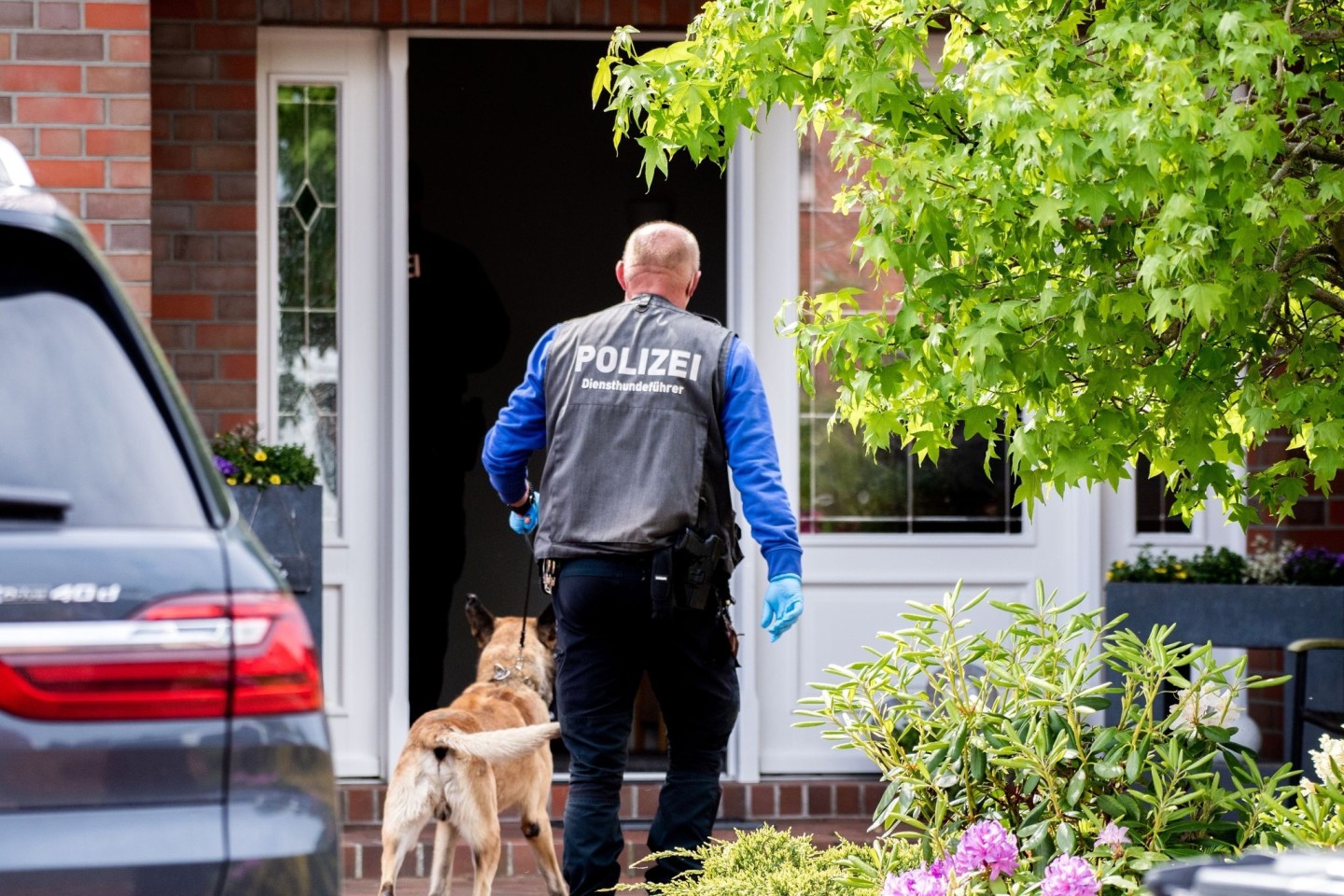 Ein Diensthundeführer der Polizei geht mit einem Spürhund zu einem Wohnhaus in Wiesmoor. Es geht um den Verdacht des Betrugs bei Corona-Hilfen.