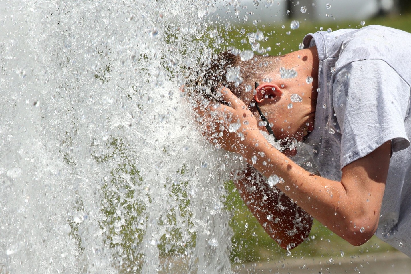 Bei Temperaturen um 29 Grad Celsius erfrischt sich ein junger Mann im Berliner Lustgarten am Wasser eines Brunnens.