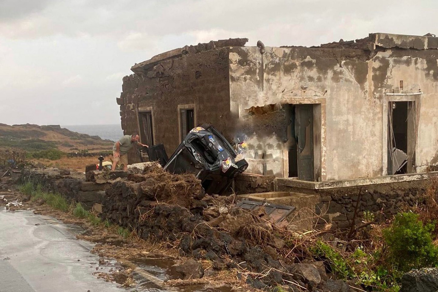 Ein zerstörtes Fahrzeug liegt abseits der Straße an einem Haus. Auf der italienischen Mittelmeerinsel Pantelleria sind zwei Menschen bei einem Unwetter ums Leben gekommen.